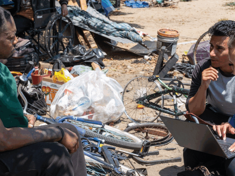 Members of the organization Healthcare in Action talk to Raylen at the encampment where he lives in Rialto on May 1, 2024. Team members had a consultation with Raylen and offered him a specialist referral.
